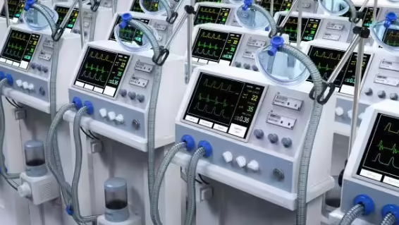 Hospital ICU ward with multiple ventilator machines displaying patient vital signs on digital monitors.