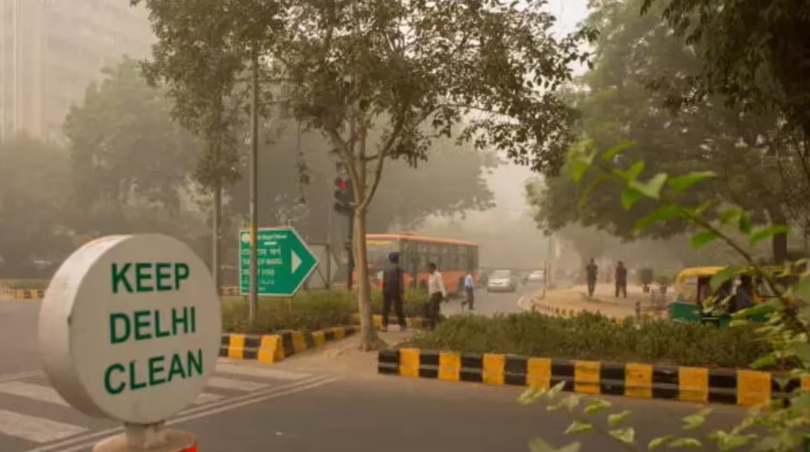 Smoggy road scene in Delhi with Keep Delhi Clean sign highlighting severe air pollution and pollution control efforts