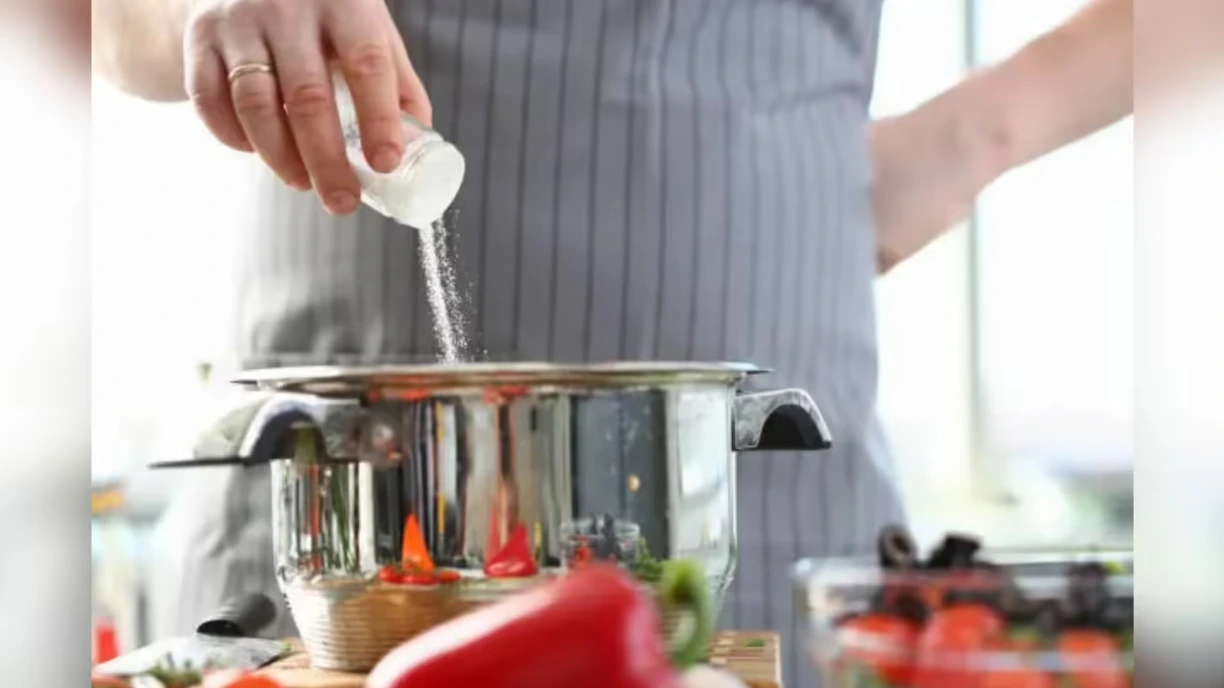 Adding salt while cooking in kitchen highlighting high sodium diet and heart health risks