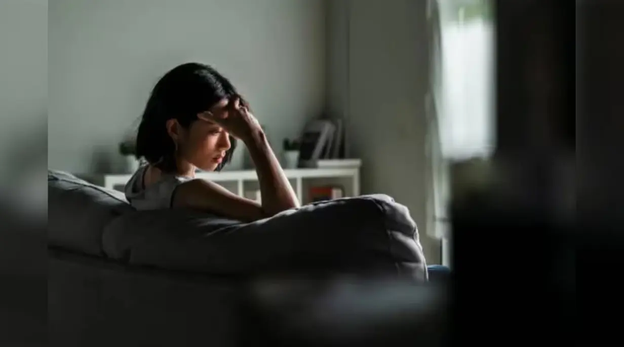 Woman sitting alone on a couch appearing stressed and emotionally overwhelmed in a dimly lit room